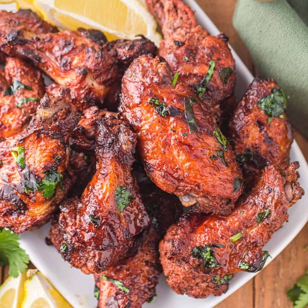 A white platter filled with glossy, red-glazed chicken wings garnished with fresh cilantro and lemon wedges.
