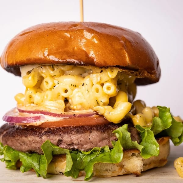 A Pijja Paradise burger with mac and cheese, red onion, tomato, and lettuce on a brioche bun.