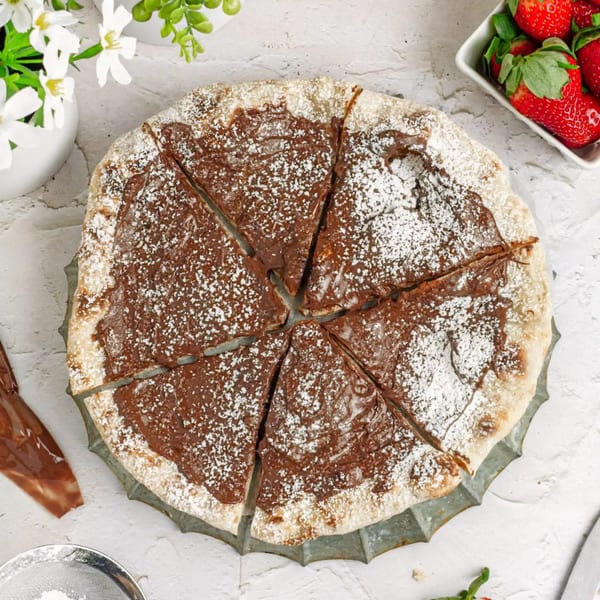 A Pijja Paradise dessert pizza with chocolate hazelnut spread and powdered sugar, sliced into six pieces.