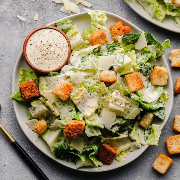 A Caesar salad with croutons, parmesan, and dressing in a small bowl on a gray plate.
