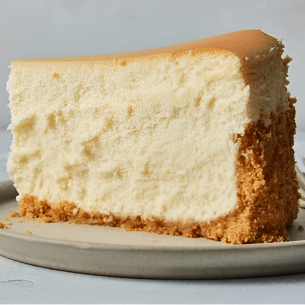 A thick slice of plain cheesecake with a graham cracker crust on a gray plate.