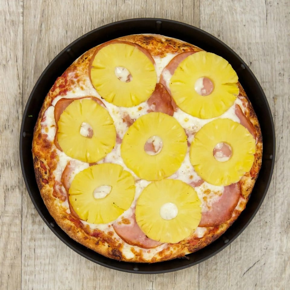 Pijja Paradise's Hawaiian pizza, topped with pineapple rings and ham, in a dark pan.