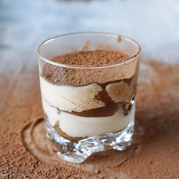 Tiramisu dessert in a glass, with layers of cream and chocolate, dusted with cocoa powder.