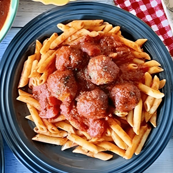 Penne pasta with meatballs and red sauce in a dark blue bowl on a rustic wooden table.