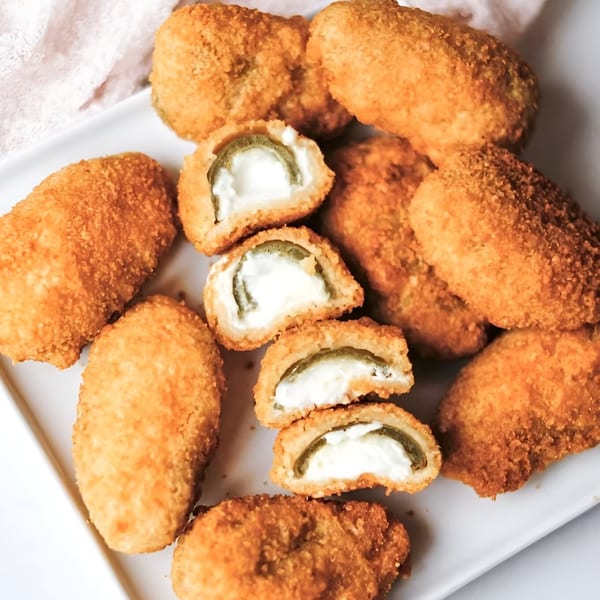 Golden-brown, breaded jalapeño poppers, some cut open to reveal creamy cheese and green pepper.